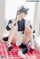 A woman in a maid outfit sitting on a red rug.