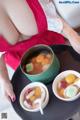 A woman in a red apron holding a bowl of soup.