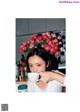 A woman holding a cup of coffee in front of a bunch of flowers.