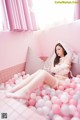 A woman in a white lingerie sitting in a pink ball pit.